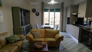 Un salon comprenant un canapé, une table basse et un téléviseur. Il y a également un coin cuisine avec des placards et une cuisinière.