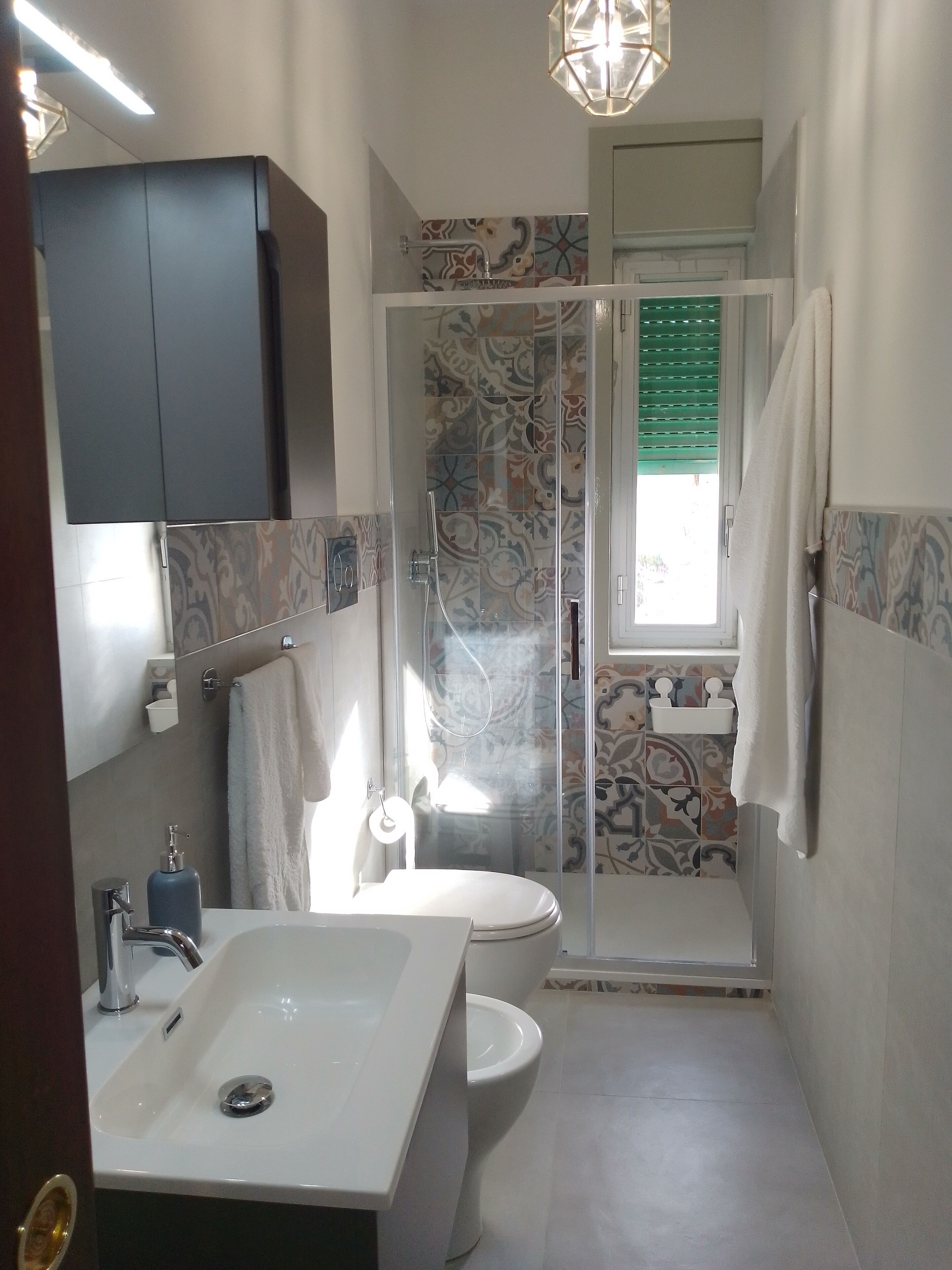 A bathroom with a white sink, toilet, and shower area. There is a mirror above the sink and a towel rack on the wall.