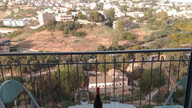 Un balcon avec une table et deux chaises, une bouteille de vin et deux verres à vin.