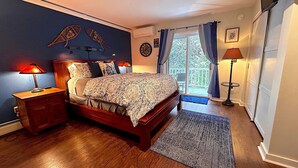 Een slaapkamer met een houten bed, twee bedlampen, een groot raam met gordijnen en uitzicht op de omgeving.
