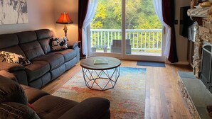 Een woonkamer met een bank, een salontafel, een open haard en een balkon met uitzicht op bomen.