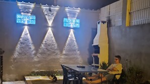A patio area with a table and chairs, a grill, and a person seated. - Ginjals_67 (Almargem do Bispo)