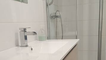 Et badeværelse med en hvid vask, en glasvægs brusekabine og et toilet.