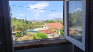 A window with a view of a residential area, including houses with red roofs and green vegetation. - Ginjals_67 (Almargem do Bispo)
