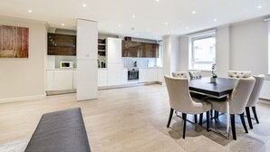 Une cuisine moderne avec des armoires blanches, un four encastré et un four à micro-ondes. On y trouve également un coin repas avec une table et des chaises.