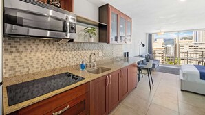 A modern kitchen with a large island, stainless steel appliances, and a view of the city through large windows. - Prime Waikiki Stay – Steps to the Beach & Dining! (Honolulu)