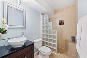 A bathroom with a white sink, toilet, and glass shower enclosure. - Prime Waikiki Stay – Steps to the Beach & Dining! (Honolulu)