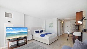 A modern bedroom with a bed, a TV, a desk, and a chair. - Prime Waikiki Stay – Steps to the Beach & Dining! (Honolulu)