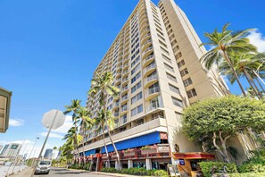 A tall hotel with multiple balconies, palm trees, and a blue awning. - Prime Waikiki Stay – Steps to the Beach & Dining! (Honolulu)