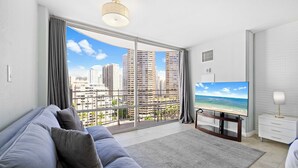 A modern living room with a large window, a flat-screen TV, and a sofa. - Prime Waikiki Stay – Steps to the Beach & Dining! (Honolulu)