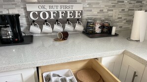 Una cocina con estación de café, utensilios en un cajón y un letrero que dice "OK, BUT FIRST COFFEE".