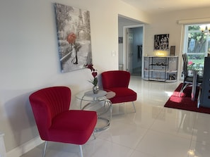 A modern living room with two red chairs, a glass coffee table, and a painting of the Eiffel Tower.
