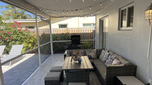 Un patio al aire libre con una mesa de madera, asientos acolchados y luces de cadena.