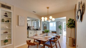 A dining area with a wooden table, chairs, and a chandelier. There are potted plants and a shelf with decorative items. - 8 Mi to Beaches: Bradenton Home w/ Poolside Oasis! (Bradenton)