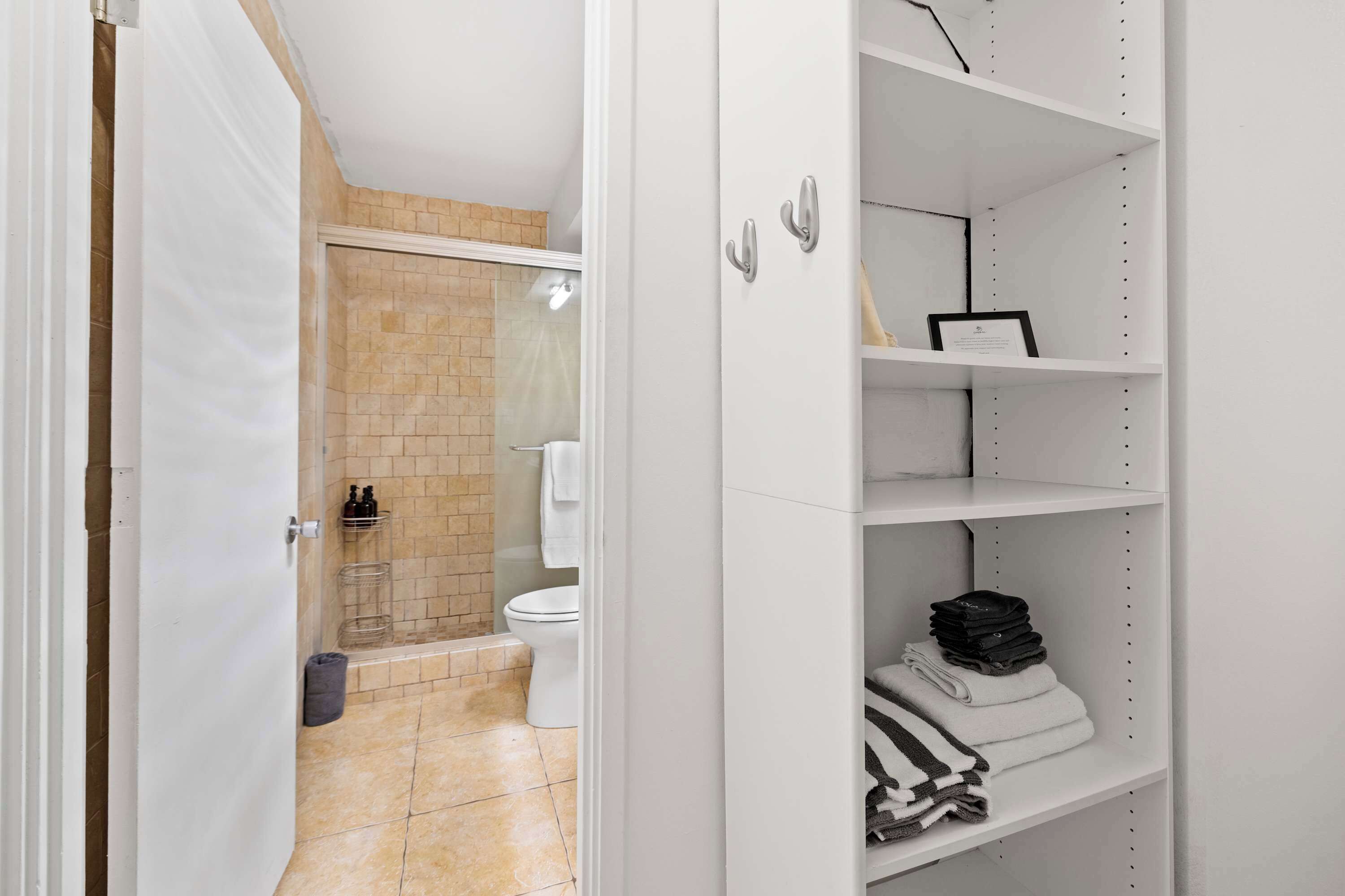 A bathroom with a shower, toilet, and a white storage unit with shelves.