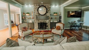 A living room with a stone fireplace, a round mirror, and a television mounted on the wall.