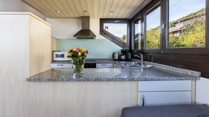 Una cocina moderna con encimeras de granito, un lavamanos de acero inoxidable, horno integrado y ventana con vistas a un barrio residencial.