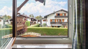 A window view of a residential area with a well-maintained lawn, a wooden deck, and a building with a balcony. - Apartment 'Kleisl' with Mountain View, Garden & Wi-Fi (Grainau)