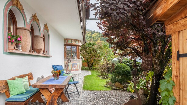 A rustic outdoor seating area with a wooden table and benches, surrounded by a gravel path and greenery. - Apartment 'Kleisl' with Mountain View, Garden & Wi-Fi (Grainau)