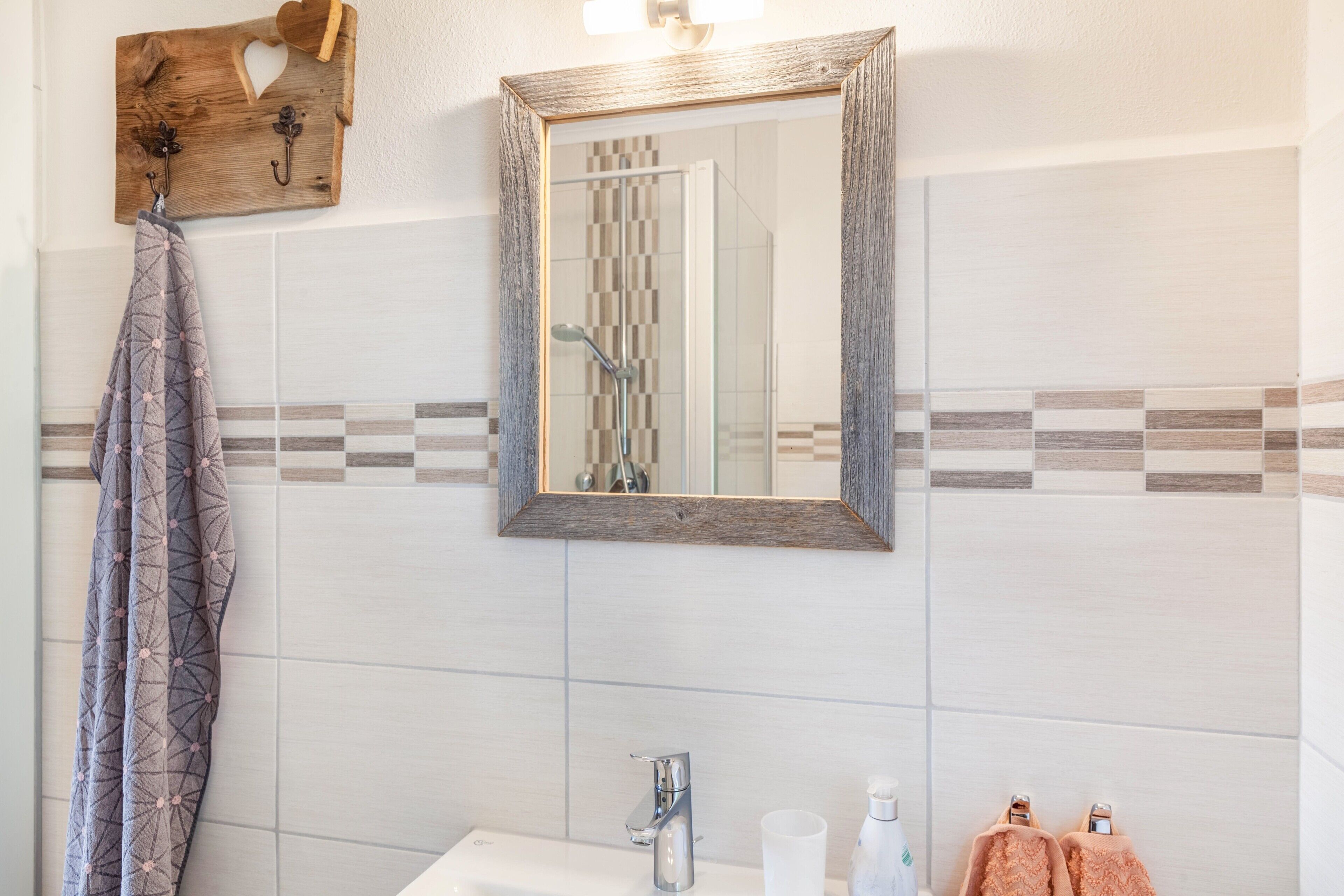 Un baño con lavamanos, espejo, toallero y azulejos estampados.