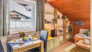 A cozy room with a dining table set for two, a comfortable sofa, a small desk with a computer, and a window with curtains. - Apartment 'Kleisl' with Mountain View, Garden & Wi-Fi (Grainau)