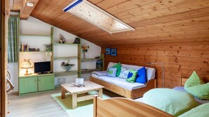 A cozy room with a wooden ceiling, a green sofa with pillows, a wooden table, and a television on a cabinet. - Apartment 'Kleisl' with Mountain View, Garden & Wi-Fi (Grainau)