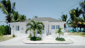 A white two-story building with a flat roof, surrounded by palm trees and a clear blue sky. - 960 Sq. ft  Beach  Front Villa located in Steventon, Exuma,  Bahamas . (Steventon)