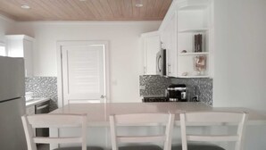 A modern kitchen with white cabinets, a wooden ceiling, and a dining area with two white chairs. - 960 Sq. ft  Beach  Front Villa located in Steventon, Exuma,  Bahamas . (Steventon)