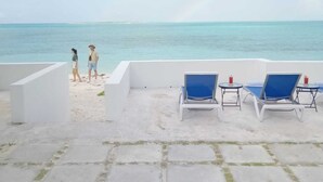 A beachside lounge with white walls, a paved area, and blue lounge chairs. - 960 Sq. ft  Beach  Front Villa located in Steventon, Exuma,  Bahamas . (Steventon)