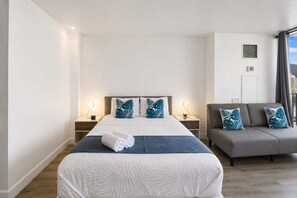 A modern hotel room with a large bed, a sofa, and a view of the city.