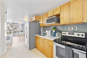 A modern kitchen with wooden cabinets, a stainless steel refrigerator, a microwave, a coffee maker, and a Whirlpool oven.