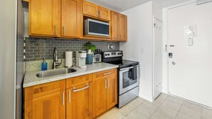 A modern kitchen with wooden cabinets, a stainless steel sink, a microwave, a coffee maker, and an oven. - Prime Waikiki Studio – Walk to the Beach! (Honolulu)