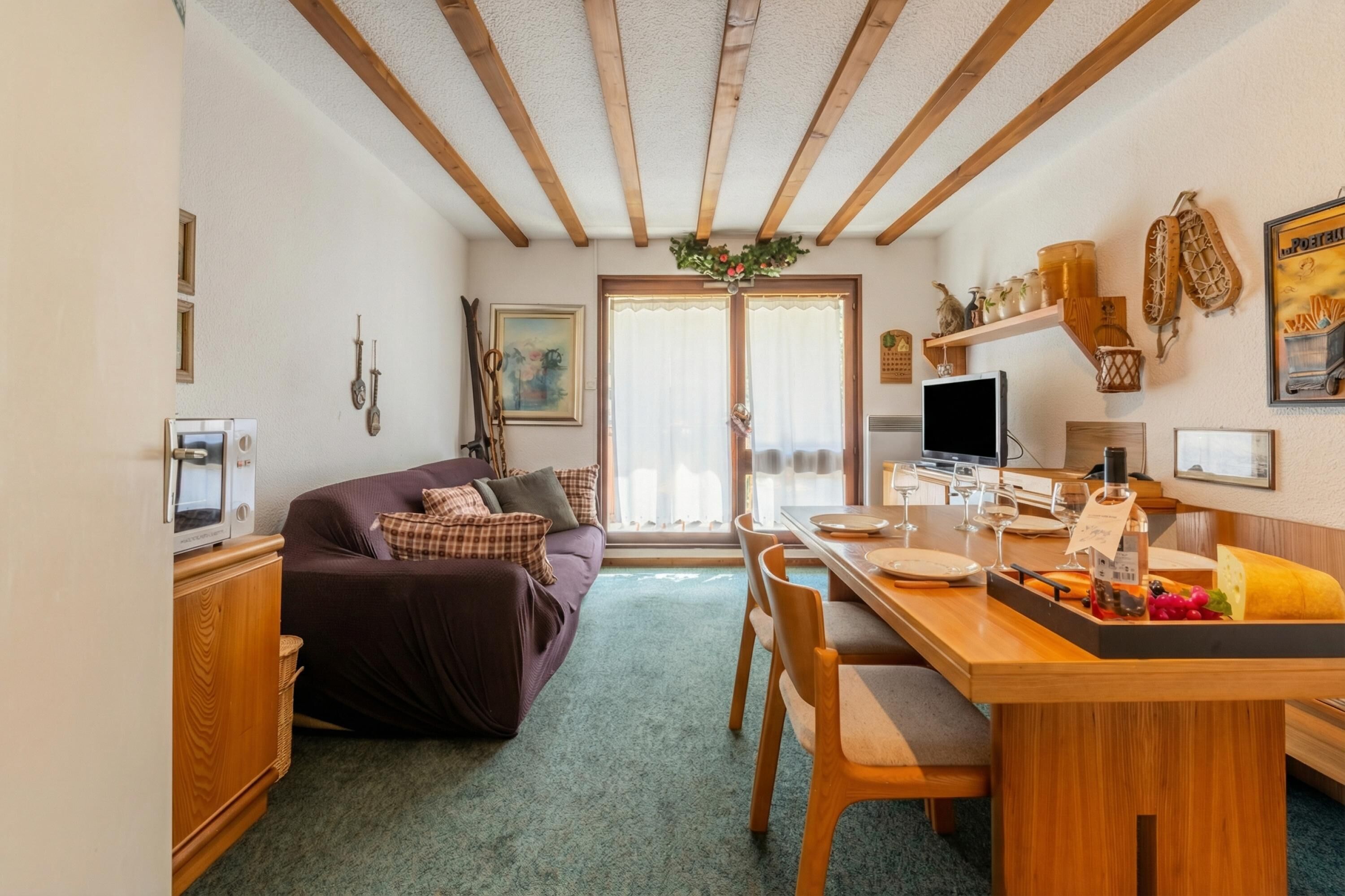 Een gezellige woonkamer met een bank, een eettafel met stoelen, een televisie en een keukenhoek met een koelkast en een magnetron.