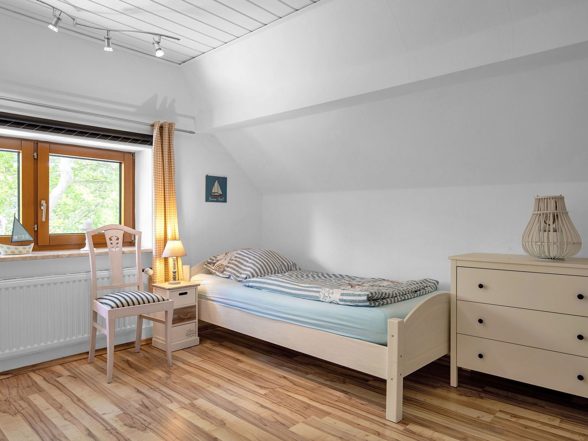 Ein Schlafzimmer mit einem Bett, einem Sessel, einer Kommode, einem Fenster mit Vorhängen und einer Heizung.