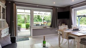 A room with a dining table, a sofa, a TV, and a view of the garden. - Beautiful private villa for 20 people with WIFI, TV, terrace and pets allowed (Bremerhaven)