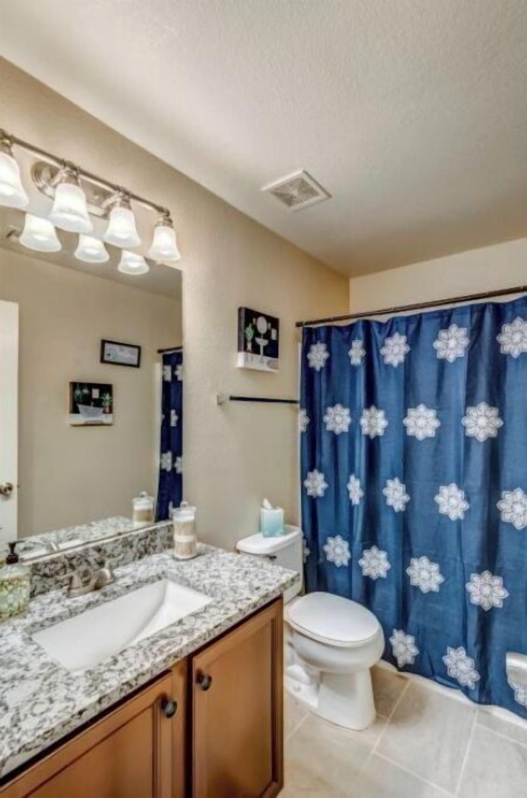 Un baño con lavamanos de mármol, inodoro blanco y cortina de ducha azul con motivos florales blancos.