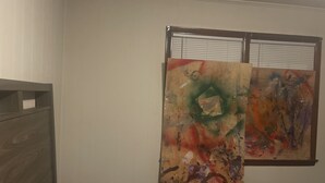 A bedroom with a bed, a window with blinds, and two abstract paintings on the wall. - BK to JAX CITY GIRL —-> COUNTRY GIRL (Jacksonville)