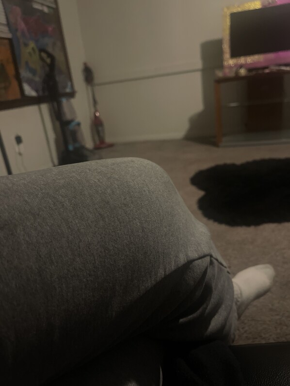 A room with a grey couch, a black rug, and a television on a stand.