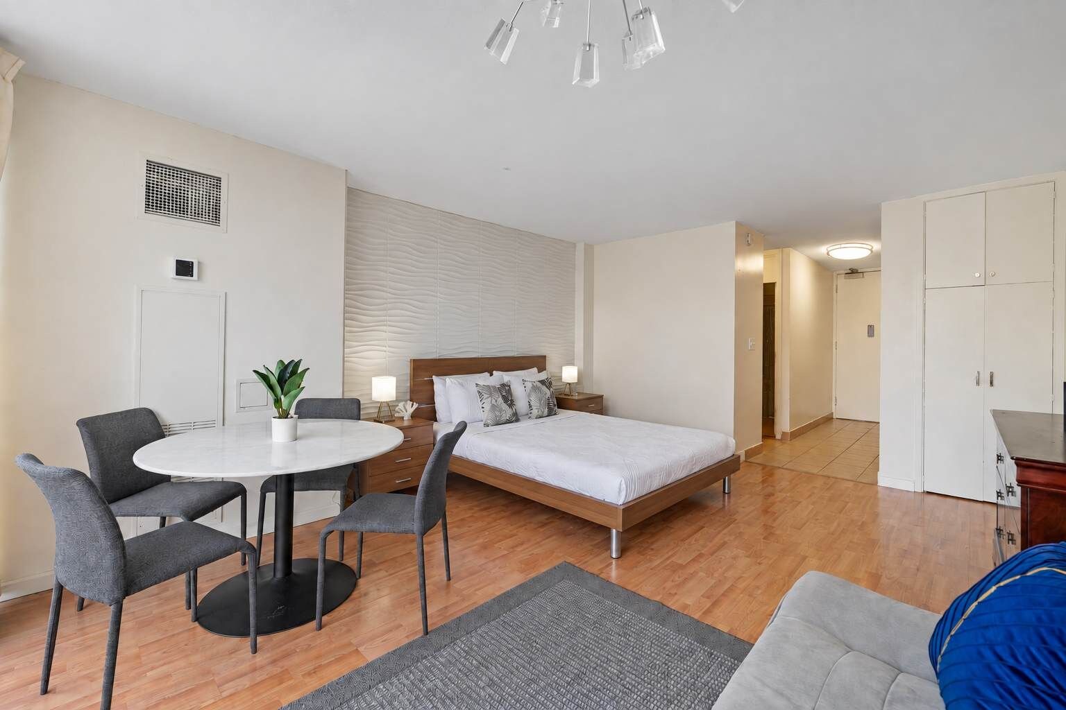 Une chambre d’hôtel avec un lit, une table de chevet, une lampe, une chaise et une petite table sur laquelle est posée une plante.