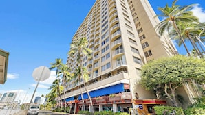 A tall hotel with multiple balconies, palm trees, and a blue awning. - Waikiki Escape – Perfect Location, Near the Beach! (Honolulu)