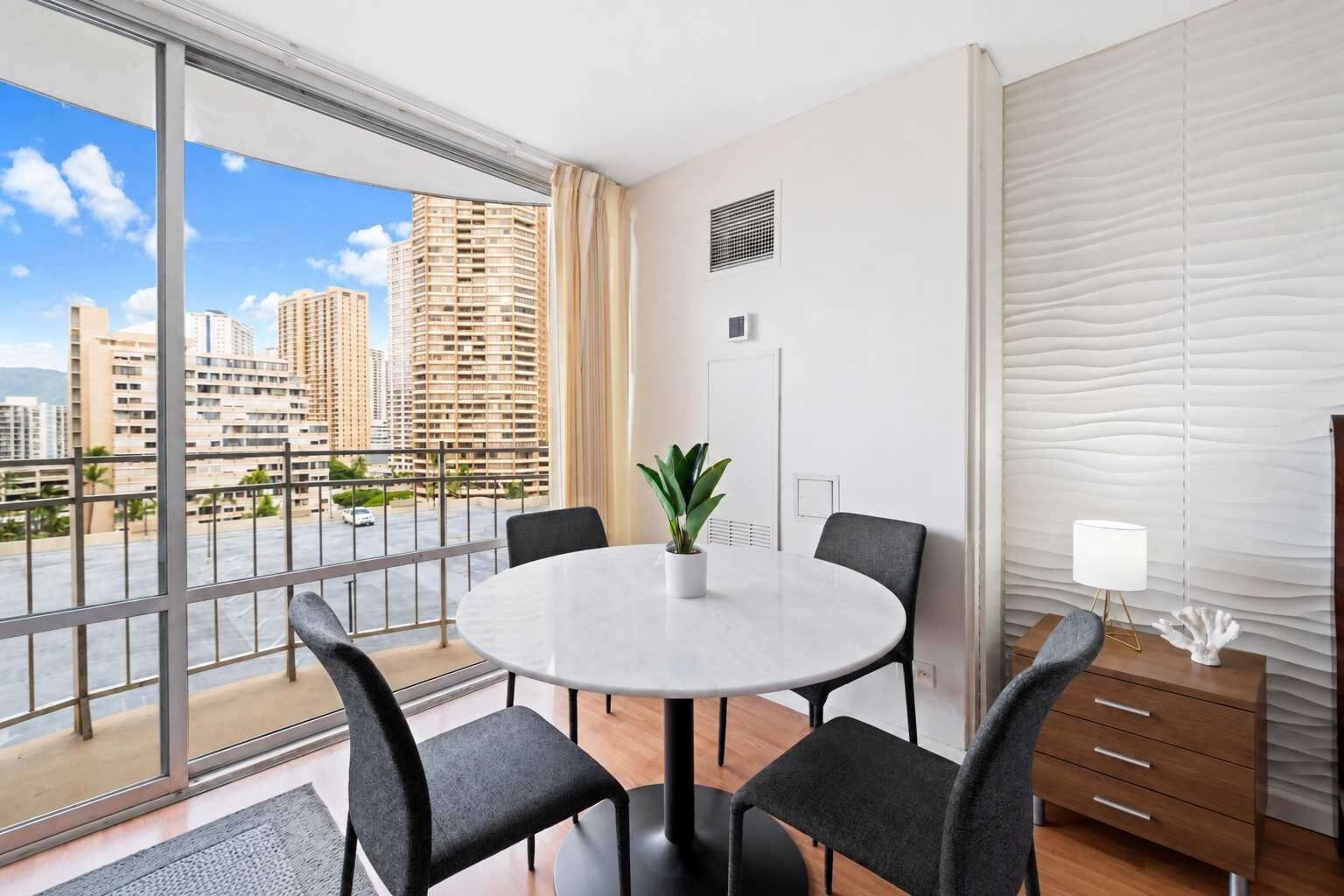 Habitación de hotel moderna con un balcón grande, una mesa de comedor redonda y vistas a la ciudad.