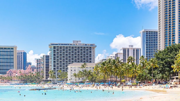A beachfront hotel with multiple high-rise buildings, palm trees, and a crowded beach. - Waikiki Escape – Perfect Location, Near the Beach! (Honolulu)