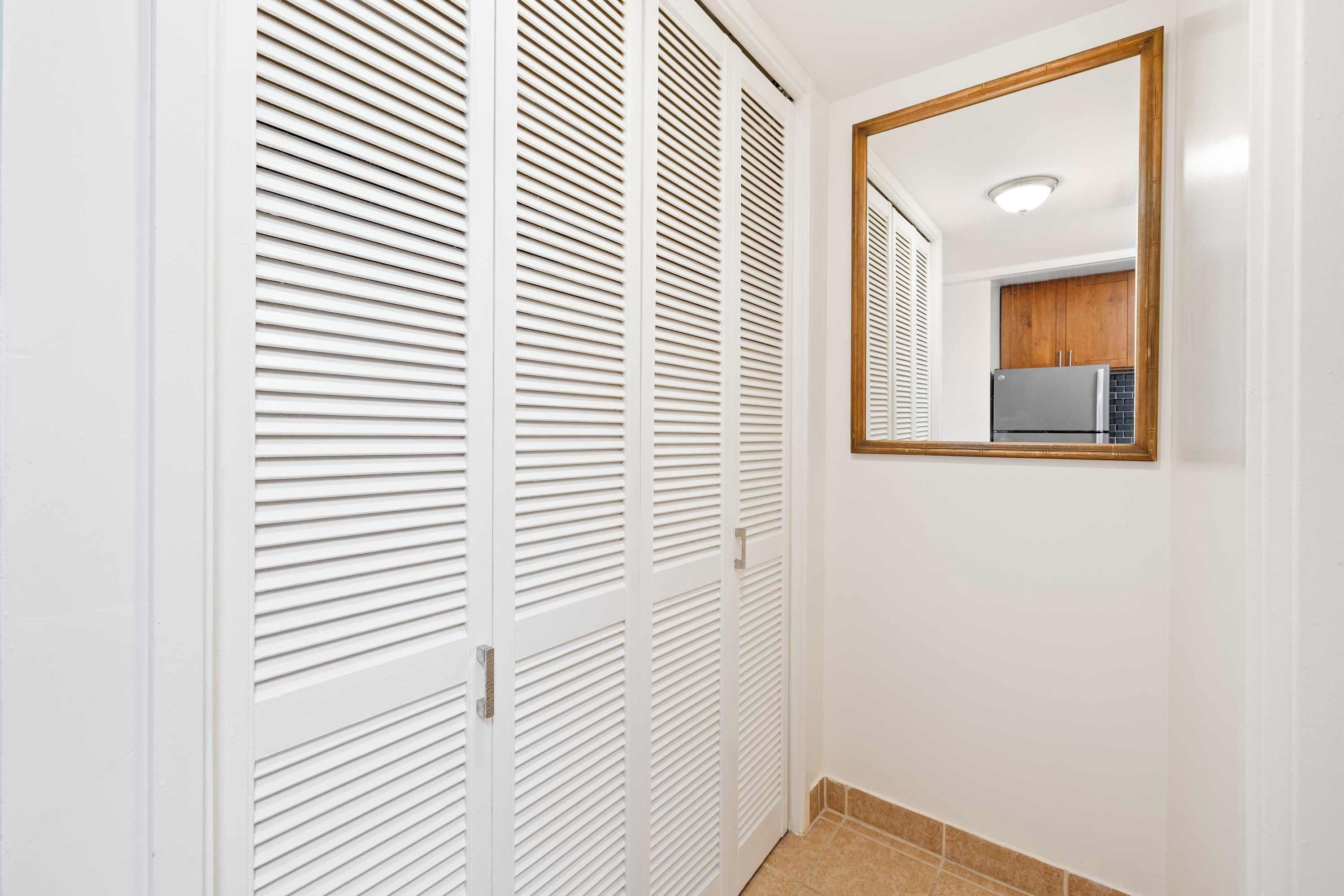 A hallway with white louvered closets and a mirror on the wall.