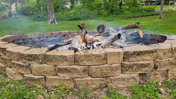 A stone fire pit surrounded by a grassy area with trees in the background.