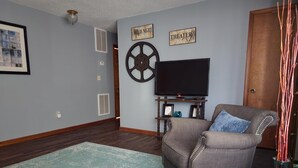 A living room with a flat-screen TV, a decorative wheel, and two signs reading "MOVIE NIGHT" and "THEATER".