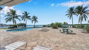 A poolside area with lounge chairs, a picnic table, and palm trees.