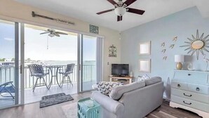 A living room with a sofa, a TV, and a balcony with chairs.
