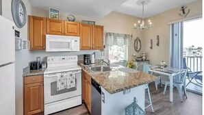 A modern kitchen with wooden cabinets, a microwave, a stove, and a sink. There is a dining area with a table and chairs.