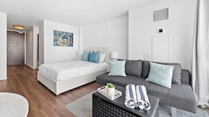 Une chambre d’hôtel moderne avec un lit, un canapé et une petite table sur laquelle se trouvent des serviettes et une plante.