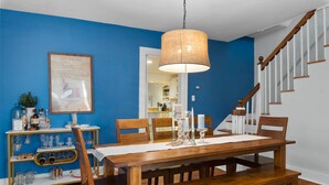 A dining area with a wooden table, chairs, a hanging light fixture, and a blue wall. - Historic Happy Home Steps from Main Street w Private Yard, Screened-In Porch & Parking (Annapolis)